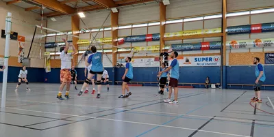 Un joueur s'élève au filet pour contrer, entouré de ses coéquipiers pendant un match en salle.