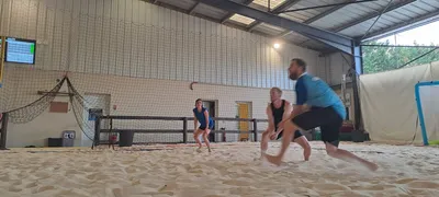 Trois joueurs en mouvement sur le sable, pendant un échange de beach-volley en salle.