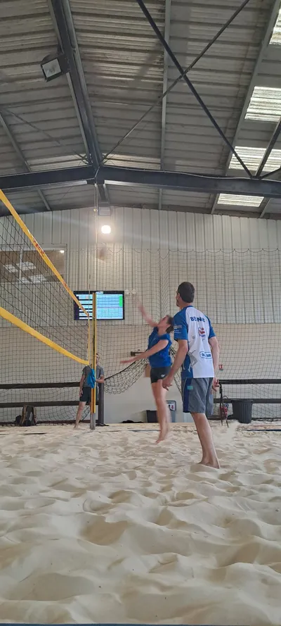 Une joueuse s'élève pour smasher au-dessus du filet, sur le terrain de beach-volley en salle.