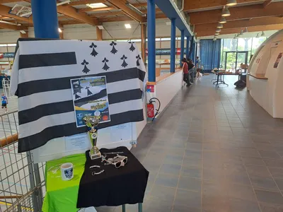 Table d'exposition avec un drapeau breton, l'affiche de la Coupe de Bretagne Finale Compét'LIB et le trophée du tournoi, entourée de goodies du club.
