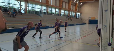 Des joueurs en maillot violet courent sur le terrain pendant un match du tournoi, sous les gradins de la salle.