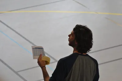 Un bénévole consulte une feuille de match, rouleau de scotch à la main, dans le gymnase.