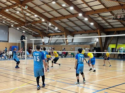 Match en cours dans la salle : une équipe en bleu affronte une équipe en jaune, sous le regard des spectateurs.