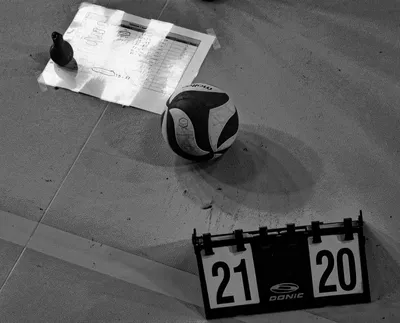 Photo noir et blanc en plongée : feuille de match, ballon et tableau de score affichant 21 à 20, au sol de la salle.